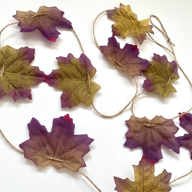 May include: A garland of faux fall leaves strung on twine. The leaves are a mix of purple, brown, and green.