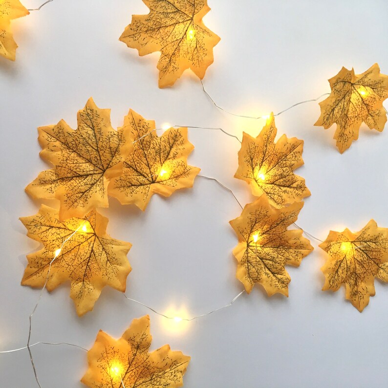May include: A string of fairy lights with yellow maple leaf cutouts. The lights are strung on a silver wire and the leaves are evenly spaced.