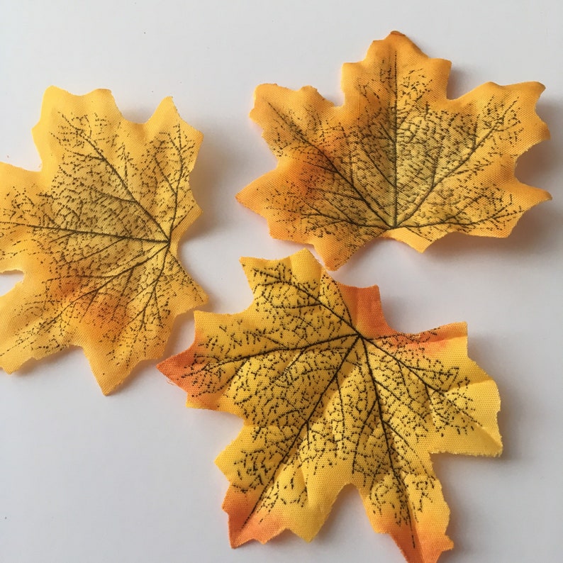 May include: Three yellow and orange fabric maple leaves with black veins. The leaves are arranged in a triangular shape.