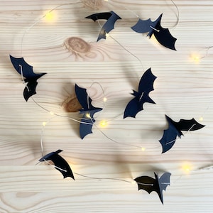 May include: A string of fairy lights with black paper bats hanging from them. The lights are strung across a light wood surface.