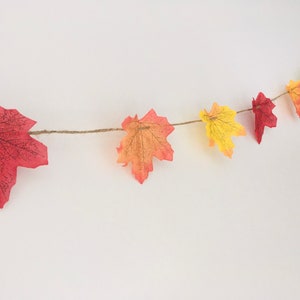 May include: A garland of fall leaves in shades of red, orange, and yellow, strung on twine.