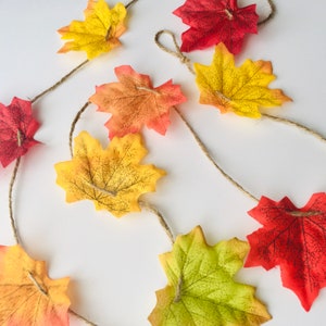 May include: A garland of fall leaves in shades of red, orange, and yellow, strung together with twine. The leaves are made of felt and have a realistic appearance.
