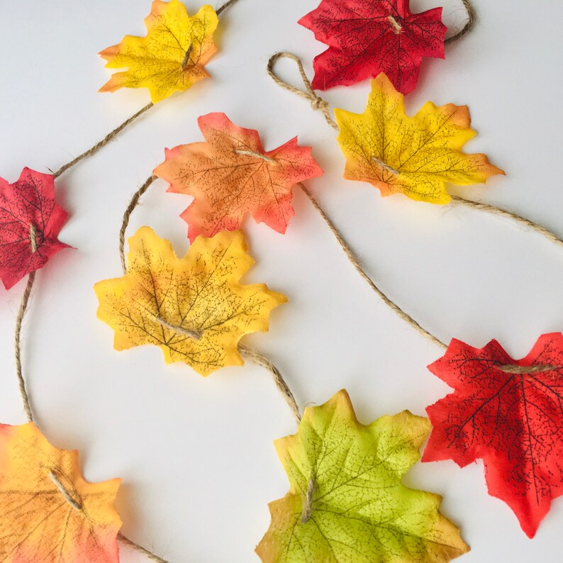 May include: A garland of fall leaves in shades of red, orange, and yellow, strung together with twine. The leaves are made of felt and have a realistic appearance.