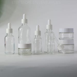 May include: Clear glass bottles and jars with white droppers and lids. The bottles vary in size and shape, with a small glass jar stacked on top of two other jars. The text "ETSY STORE STEVENSUPPLIES" is at the top.