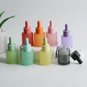 May include: A set of ten frosted glass dropper bottles with colourful caps. The bottles are arranged in a row on a white surface. The bottles are all the same size and shape, and they have a frosted finish. The caps are all different colours, including pink, orange, yellow, green, and purple.