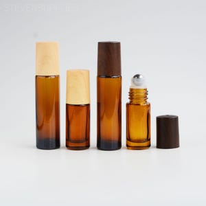 May include: Several amber glass essential oil bottles with wooden and dark brown caps are displayed. One bottle has a silver rollerball top. The bottles vary in size and shape, all with a dark base.