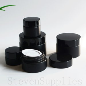 May include: Five black frosted glass jars with black lids. The jars are of different sizes and are arranged in a pyramid shape. The top jar is open and has a white plastic lid inside.