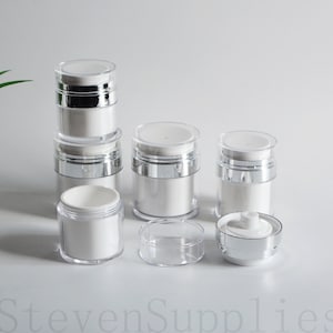 May include: A set of six clear and white plastic pump bottles with silver caps. The bottles are stacked and arranged on a white surface.