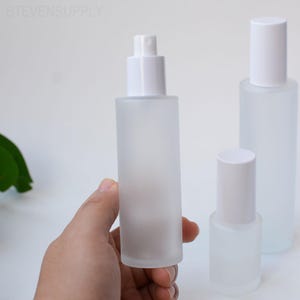 May include: Three frosted glass bottles with white tops. One bottle has a spray nozzle, and the other two have cylindrical caps. The bottles are different sizes and are set against a white background. The text "STEVENSUPPLY" is visible at the top.