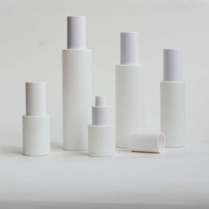 Könnte beinhalten: Eine Sammlung weißer Kosmetikflaschen und -behälter mit weißen Deckeln. Die Flaschen variieren in Größe und Form, einschließlich zylindrischer und abgerundeter Designs. Das Bild ist vor einem schlichten weißen Hintergrund.