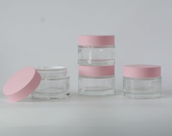 May include: Four clear glass jars with pink lids. The jars are different sizes and are stacked on top of each other. The jars are perfect for storing small items, such as jewelry, cosmetics, or craft supplies.