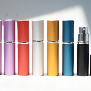 Peut inclure: Un ensemble de sept flacons vaporisateurs de parfum cylindriques dans diverses couleurs mates, notamment rose, violet, rouge, argenté, doré, bleu et noir. Chaque flacon dispose d'un capuchon amovible assorti et d'un mécanisme de pulvérisation argenté.