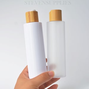 May include: Two cylindrical bottles with bamboo lids. One bottle is white, the other is frosted. The bottles are held in a hand against a white background. The text "STEVENSUPPLIES" is at the top of the image.