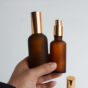 Op de afbeelding: Twee bruine glazen spuitflessen met goudkleurige sproeikoppen. De flessen hebben een matte afwerking. De tekst "STEVENSUPPLIES" is zichtbaar bovenaan de afbeelding.