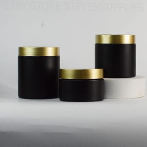 Peut inclure: Trois bocaux cylindriques noirs avec des couvercles dorés. Les bocaux sont de tailles variables et sont disposés sur une surface blanche. Les bocaux ont une finition mate. Le texte "ETSY STORE STEVENSSUPPLIES" est visible en haut de l'image.