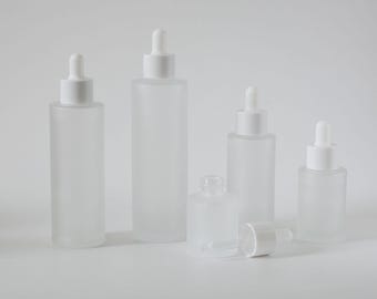 May include: Five frosted glass bottles with white dropper tops. The bottles are different sizes and are arranged in a row from largest to smallest.