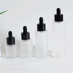 May include: Four frosted glass bottles with black dropper tops. The bottles are of different sizes and are arranged in a row from smallest to largest.