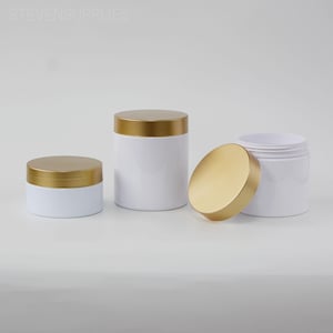 Könnte beinhalten: Weiße Kosmetikgläser mit goldenen Deckeln. Die Gläser sind zylindrisch und in verschiedenen Größen erhältlich. Ein Glas hat seinen Deckel abgenommen, wodurch das Innere sichtbar wird. Der Text "STEVENSUPPLIES" ist in der oberen linken Ecke zu sehen.