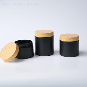 May include: Three cylindrical containers with matte black bodies and light-coloured wood grain lids. One lid is placed beside an open container, while two containers are closed. The text STEVENSUPPLIES is visible in the upper left corner.