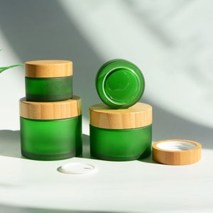 Könnte beinhalten: Vier grüne Glasbehälter mit Bambusdeckeln. Die Behälter sind matt und haben eine matte Oberfläche. Die Deckel sind aus natürlichem Bambus.