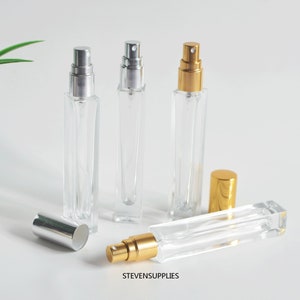 May include: Three clear glass bottles with silver and gold spray tops. The bottles are rectangular and have a square base. The bottles are empty and ready to be filled with perfume or essential oils.