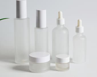 May include: A collection of frosted glass cosmetic containers with white lids. The set includes various sizes of bottles and jars, suitable for skincare products. The containers are arranged on a white surface.