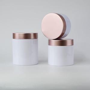 May include: Three white jars with rose gold lids. The jars are stacked on top of each other.