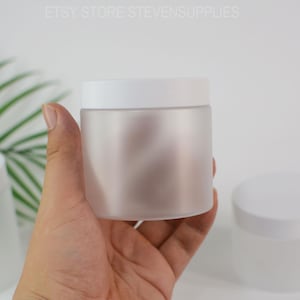 Puede incluir: Un tarro de vidrio esmerilado con tapa blanca se sostiene en una mano. El tarro cilíndrico tiene un acabado liso y opaco. La tapa encaja a ras. El texto "ETSY STORE STEVENSSUPPLIES" es visible en la parte superior.