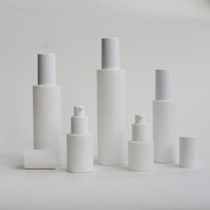 May include: An assortment of white cosmetic bottles and containers, featuring white pump dispensers and caps. The bottles are in various sizes and shapes, ideal for skincare products. The image is well-lit, showcasing the clean design of the packaging.