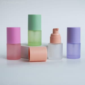 May include: A selection of frosted glass cosmetic bottles with coloured lids and a pump dispenser. The bottles are in shades of pink, green, peach, and purple. The image is set against a white background.