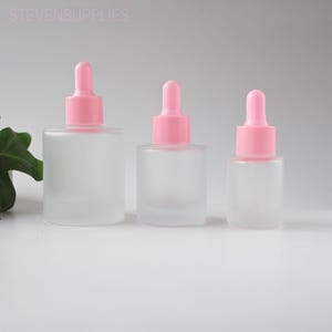 May include: Three frosted glass dropper bottles with pink tops. The bottles are in varying sizes, with a square base and a rounded top. The text "STEVENSUPPLIES" is visible at the top of the image.