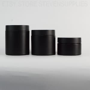 Puede incluir: Tres tarros cilíndricos negros mate con tapas a juego de diferentes tamaños. Los tarros están dispuestos en fila, el más grande a la izquierda y el más pequeño a la derecha. Los tarros están vacíos y listos para ser llenados.