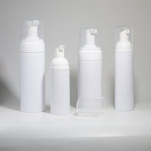 May include: Four white foam pump bottles of different sizes are displayed. Each bottle has a white pump and a clear plastic cap. The bottles are cylindrical and appear empty, ready for filling with liquid. The bottles are on a white surface.