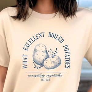 May include: A cream-coloured t-shirt with a blue graphic that says "What Excellent Boiled Potatoes" with a drawing of two potatoes and the text "Exemplary Vegetables Est. 1813".