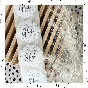 Könnte beinhalten: Vier weiße runde Aufkleber mit schwarzem Text und schwarzen Punkten. Die Aufkleber sagen "eine Portion Glück für dich", was "eine Portion Glück für dich" bedeutet.
