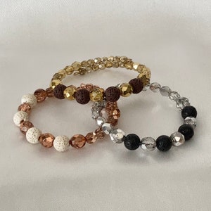 May include: Three beaded bracelets with brown, gold, and silver beads. The bracelets are made of lava rock and glass beads.