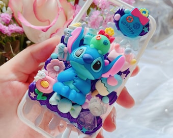 May include: A clear phone case with a blue Stitch character, pink, purple, and white 3D embellishments, and a purple and white dripping design.