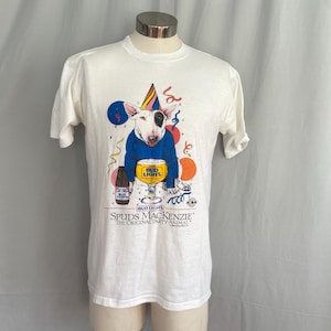 May include: Off-white t-shirt featuring a cartoon Bull Terrier wearing a party hat and blue sweater, with balloons and a Bud Light beer bottle and glass. The text reads "Bud Light" and "Spuds MacKenzie The Original Party Animal."