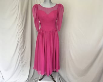 May include: A pink chiffon dress with a sweetheart neckline and puffed sleeves. The dress has a gathered skirt and a sheer overlay at the neckline.