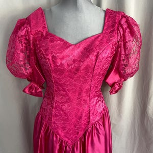 May include: A bright pink formal dress with a square neckline and lace bodice. The dress features puffy lace sleeves and a satin skirt. The dress is displayed on a mannequin.