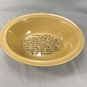 May include: A light yellow ceramic serving bowl with a handwritten recipe for "Country Supper" inside. The recipe includes instructions for cooking chicken, tomatoes, and onions. The bowl has a wide rim and a slightly oval shape.