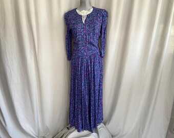 May include: A vintage floral print dress in shades of blue, purple, and teal. The long-sleeved dress features a pleated skirt and a white lace collar. The dress is displayed on a mannequin.