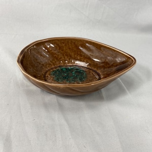 May include: A brown, leaf-shaped ceramic bowl with a textured exterior and a glossy finish. The interior features a speckled, teal-colored design. The bowl is likely used for serving or display.