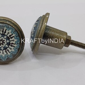 May include: Two antique brass cabinet knobs with a blue and white floral design. The knobs have a screw-on back.