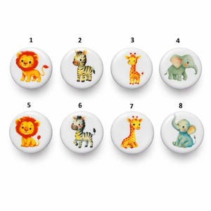 Könnte beinhalten: Acht weiße, runde Knöpfe mit Aquarellillustrationen von Safari-Tieren. Die Designs umfassen einen Löwen, ein Zebra, eine Giraffe und einen Elefanten in verschiedenen Posen und Farben. Ideal für Bastelprojekte.