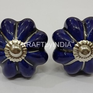 May include: Two blue ceramic flower-shaped cabinet knobs with silver accents.