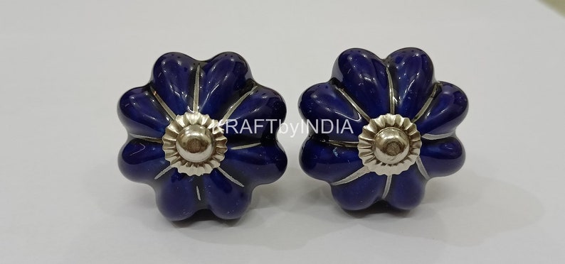 May include: Two blue ceramic flower-shaped cabinet knobs with silver accents.