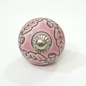 May include: Pink ceramic knob with a floral design and a silver metal center. The knob is round and has a smooth surface.
