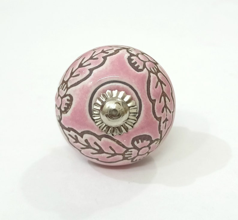 May include: Pink ceramic knob with a floral design and a silver metal center. The knob is round and has a smooth surface.
