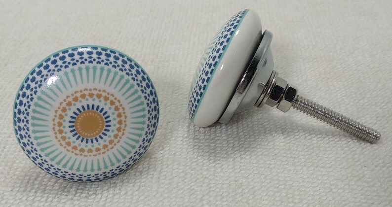 May include: Two ceramic cabinet knobs with a blue, white, and orange geometric pattern. The knobs have a silver metal base and a screw for attaching to a cabinet door.